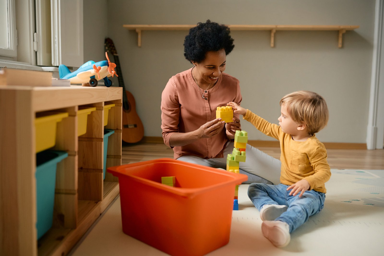 Happy black teacher and small boy playing with toy blocks at kindergarten, Behavioral Therapy